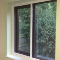 Horizontal sliding fly screens on a brown uPVC window